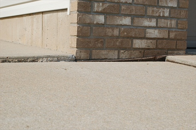 Sunken concrete slab next to a brick foundation showing the need for concrete raising